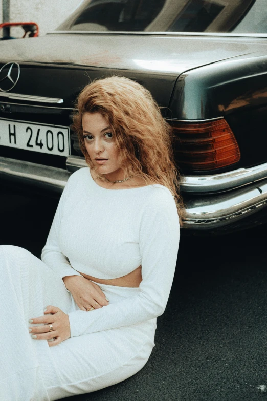 a woman sitting in front of a mercedes car