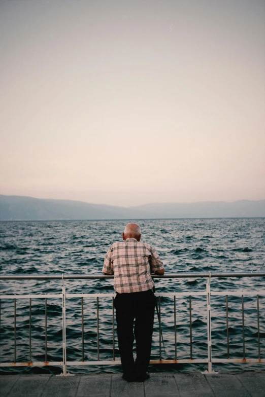 an elderly man standing on the edge of a metal railing next to the ocean