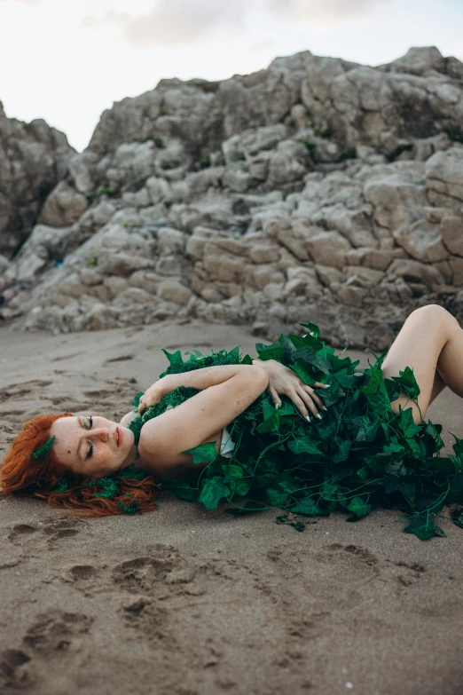 a redhead haired woman laying on the beach surrounded by green ivy