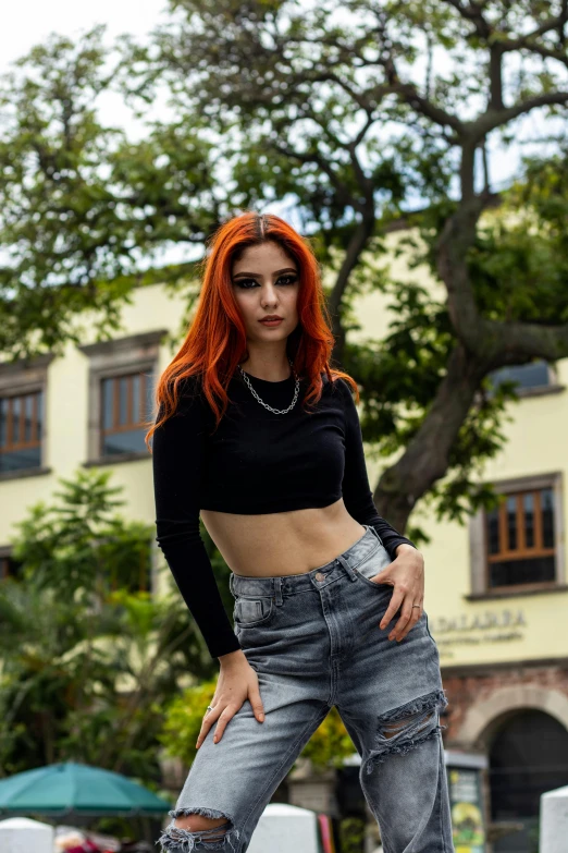 a red headed girl with long orange hair standing in a black crop top and jeans