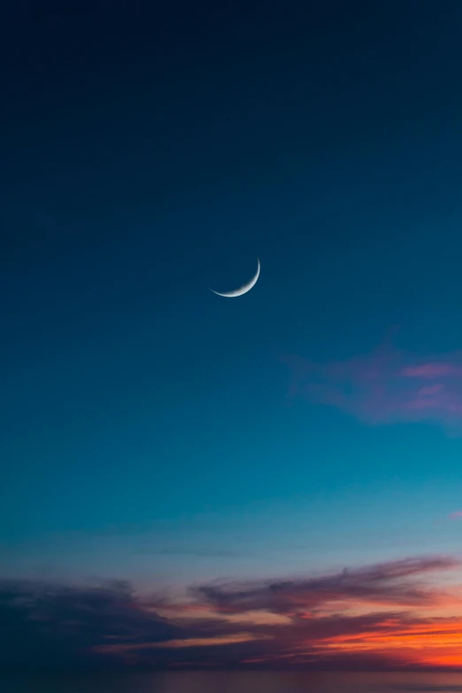 a crescent shaped moon hangs in a blue sky