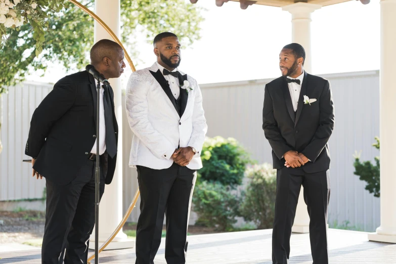 a group of men standing around each other wearing tuxedos