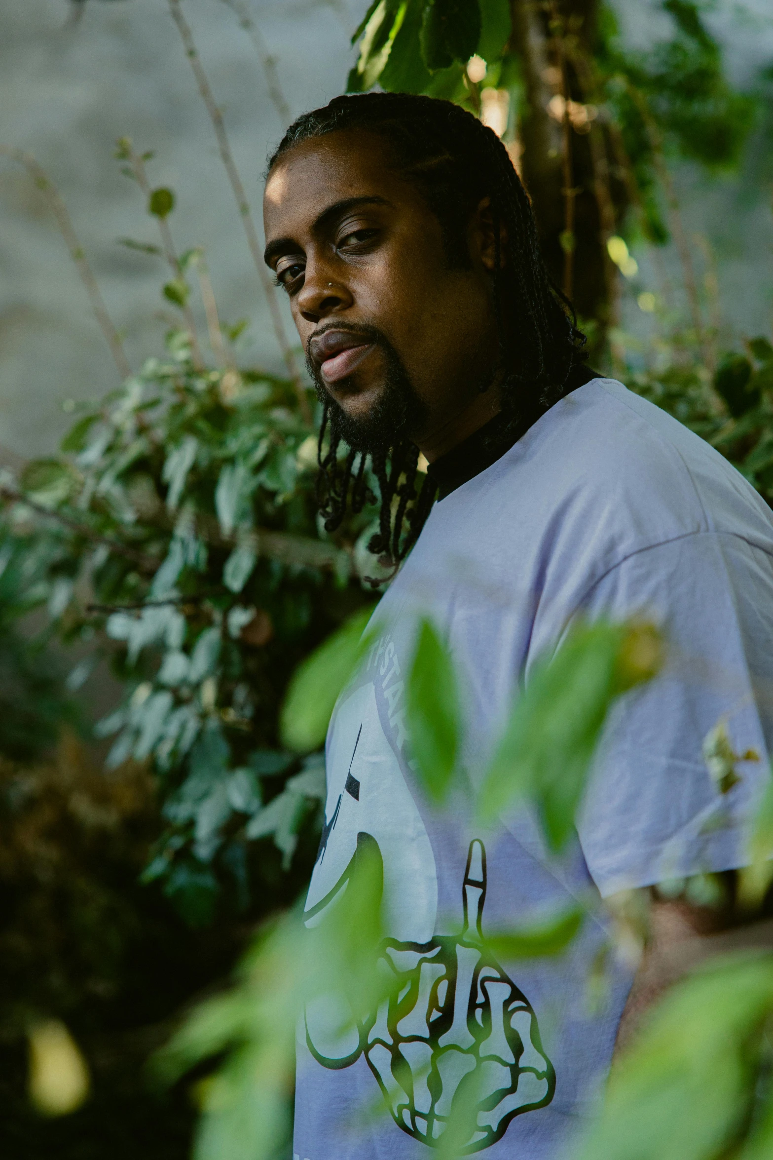 a man with long dreadlocks standing in front of some green plants