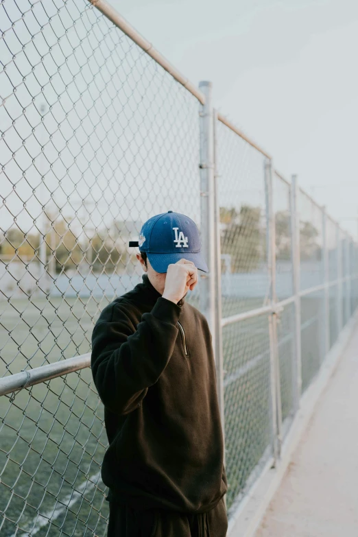 a man leaning against a fence with a baseball cap