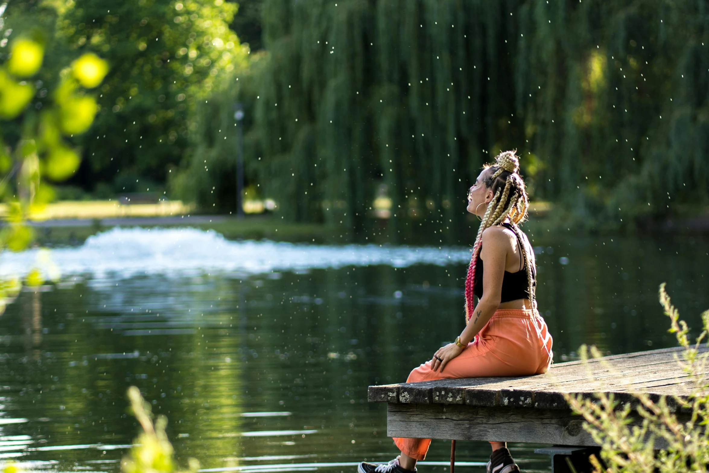 a woman sitting on the edge of a dock by a lake