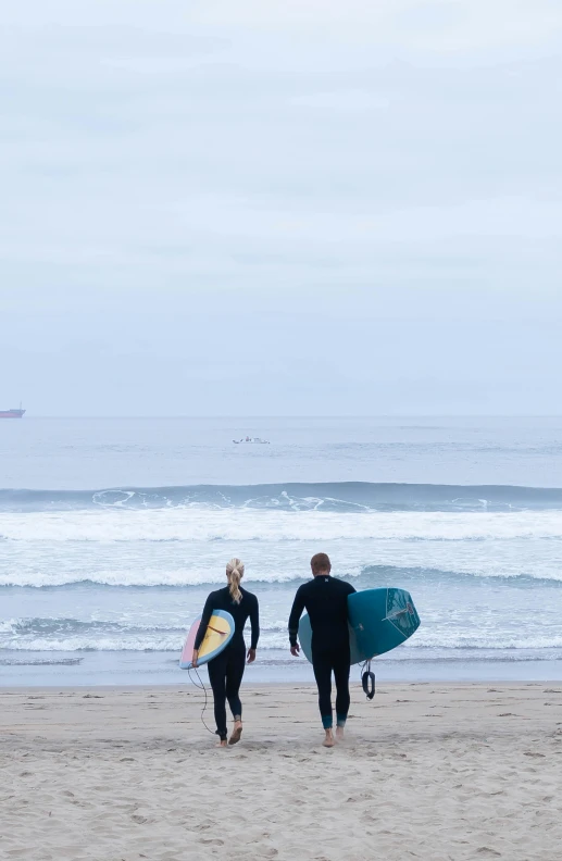 two people walking along the beach with surf boards