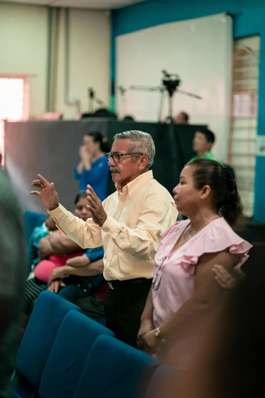 a man standing next to a blue chair in front of a crowd