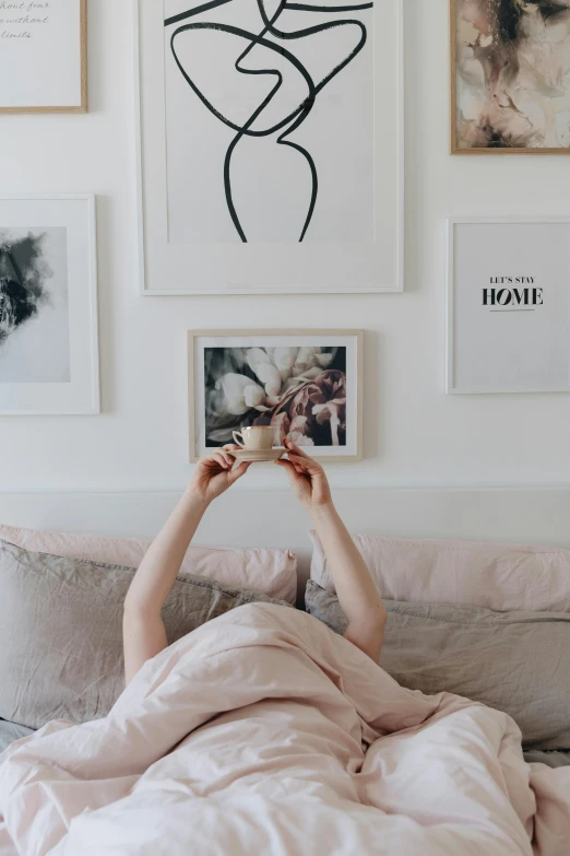 woman laying in bed holding up cup of coffee