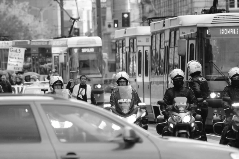 a group of motorcyclist standing behind a bus on the street