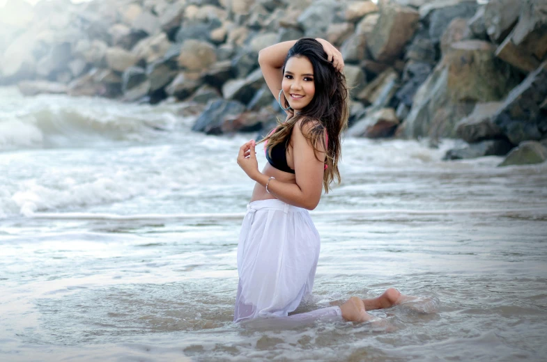 a pretty young lady standing in the surf at the beach