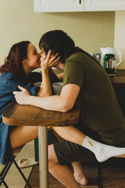 two people kissing each other while sitting at a table