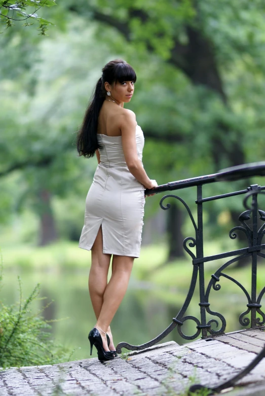 a young woman in high heels and dress leaning against a railing