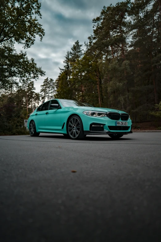 a turquoise bmw car parked in the middle of a road