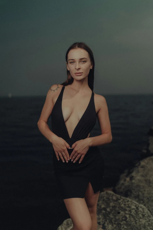 a woman wearing a black one piece standing by the ocean