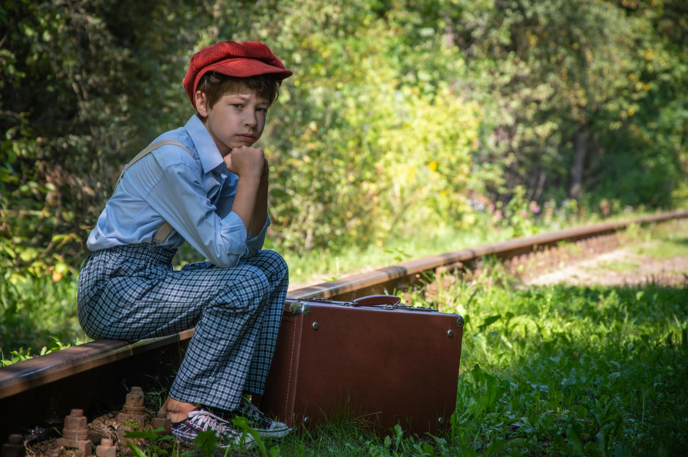 boy sitting on railway tracks and looking bored