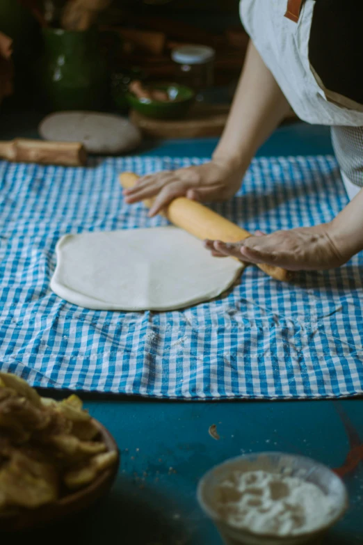 a woman is rolling bread on a blue and white tablecloth