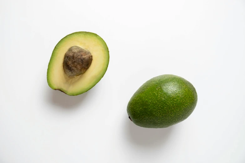 the green avocado is sitting next to the one on the table