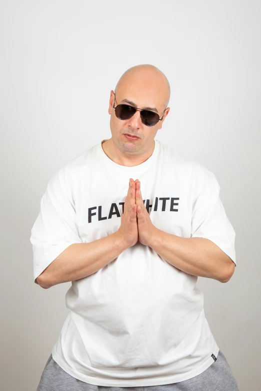 the bald man wearing a shirt and shades has his hands folded up
