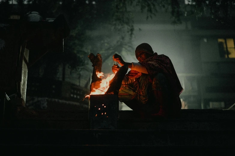 someone sitting next to an open fire pit while holding onto soing