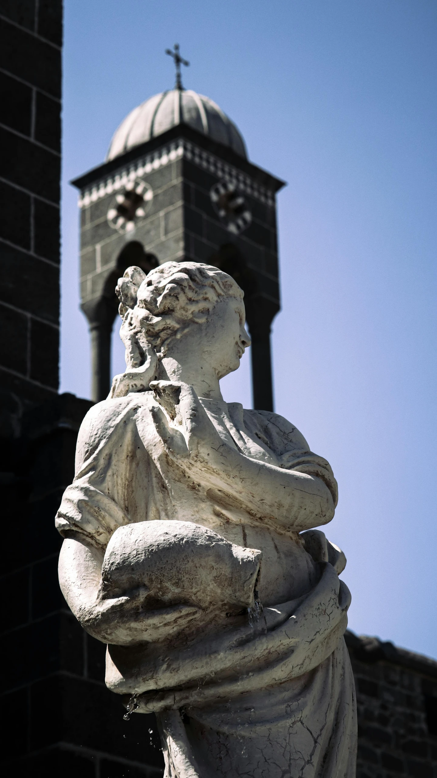 the statue is by a brick building and a steeple