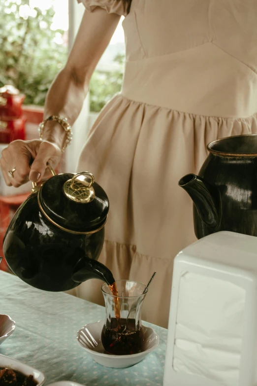 a woman in dress pouring tea at a table