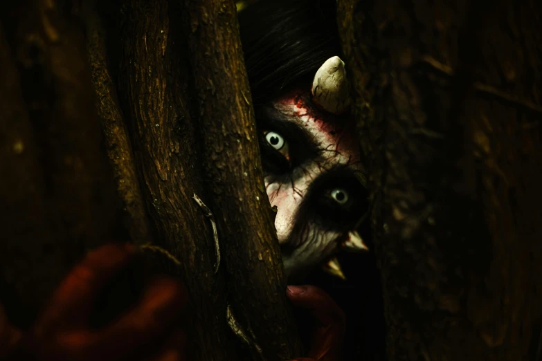 a scary mask peeking out from behind a tree trunk