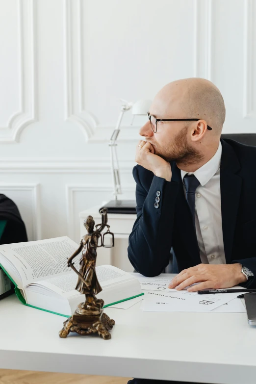 a bald man in suit sitting at desk and looking at book