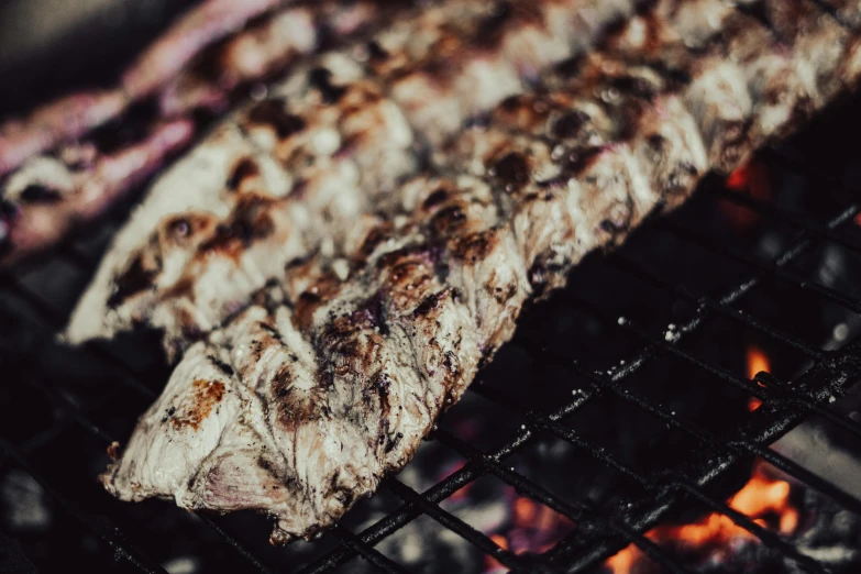 steak cooking on the grill with dark flames in the background