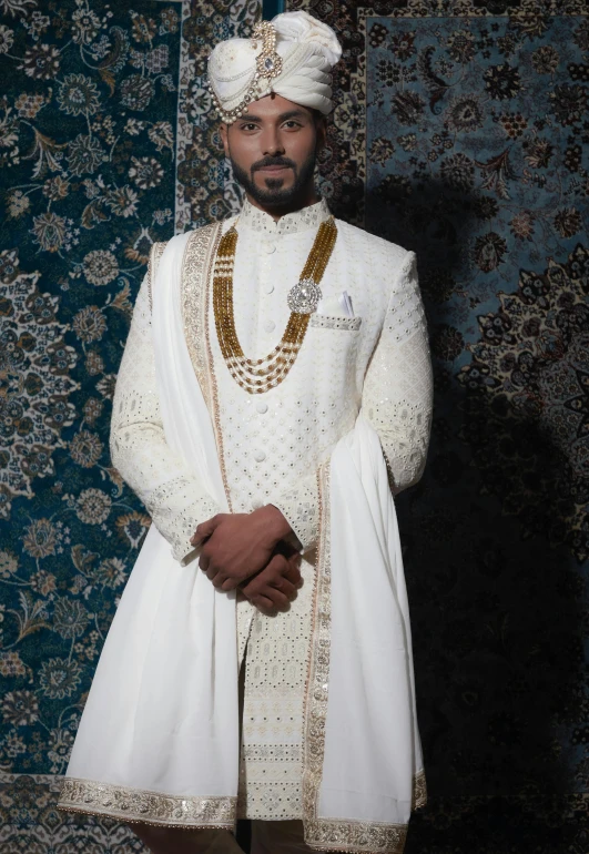 a man standing in front of a blue wall wearing an outfit with golden chains and a head scarf