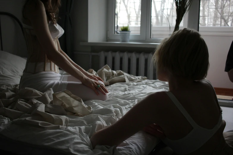 two women reaching for a white dress on the bed