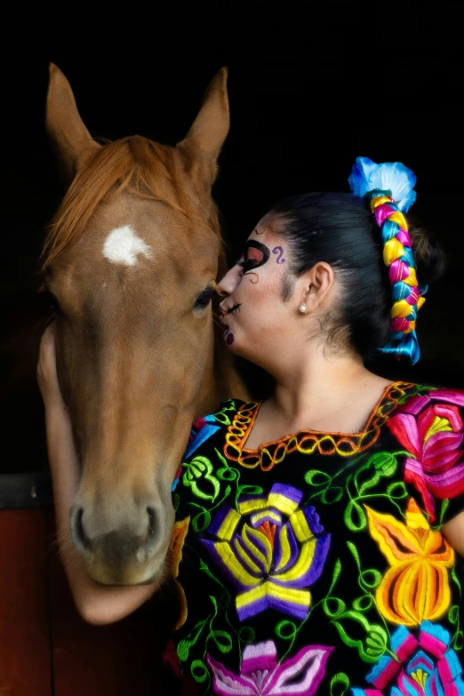 a woman dressed in brightly colored clothing is kissing a brown horse