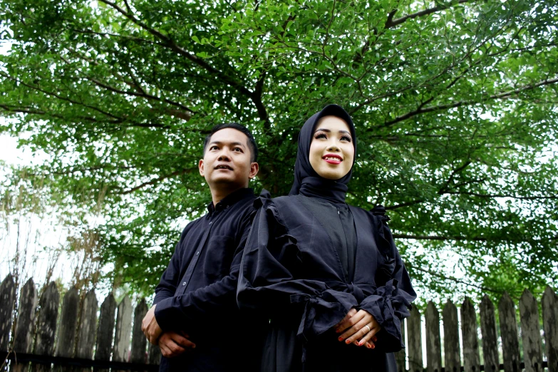 a man and woman wearing black posing for a po under a tree