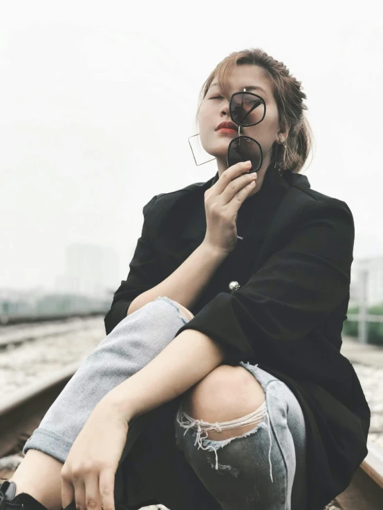 a woman with glasses is sitting on the train tracks