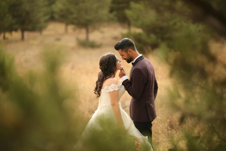 a bride and groom hold each other in a field with trees