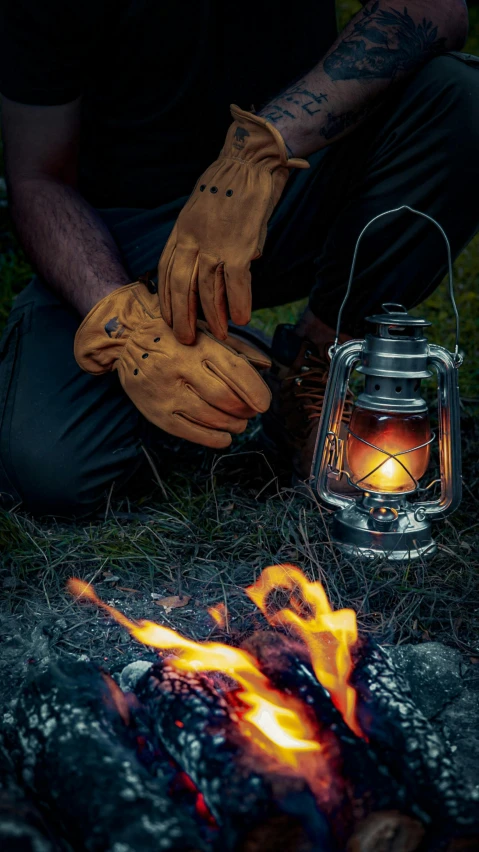 a man with gloves and burning hand next to lantern