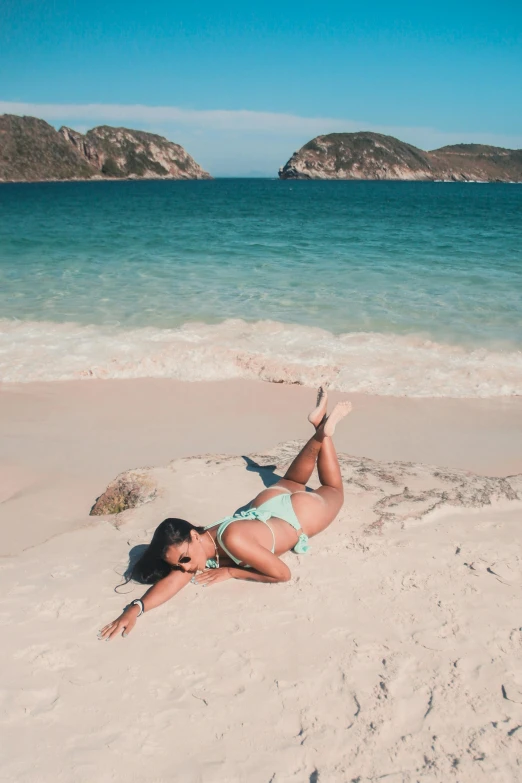 a woman is lying on the sand near the water