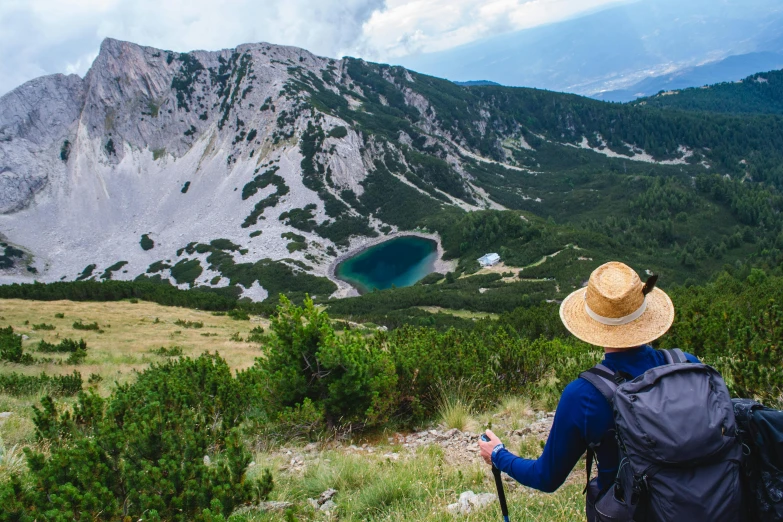 a hiker stands at the top of a steep hill looking at a large lake