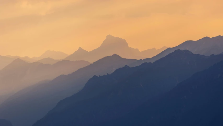 mountains are silhouetted by the yellow light of sunrise