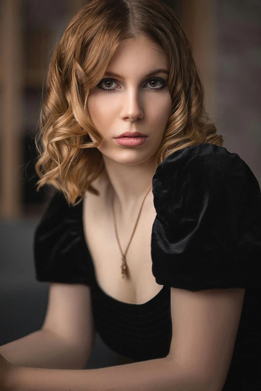 a woman with a necklace on sitting and posing for a portrait