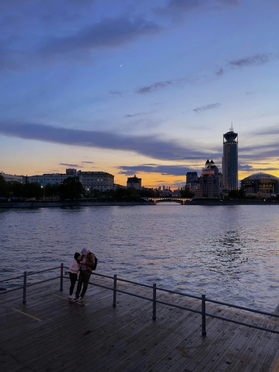 two people are standing on a dock near the water at sunset