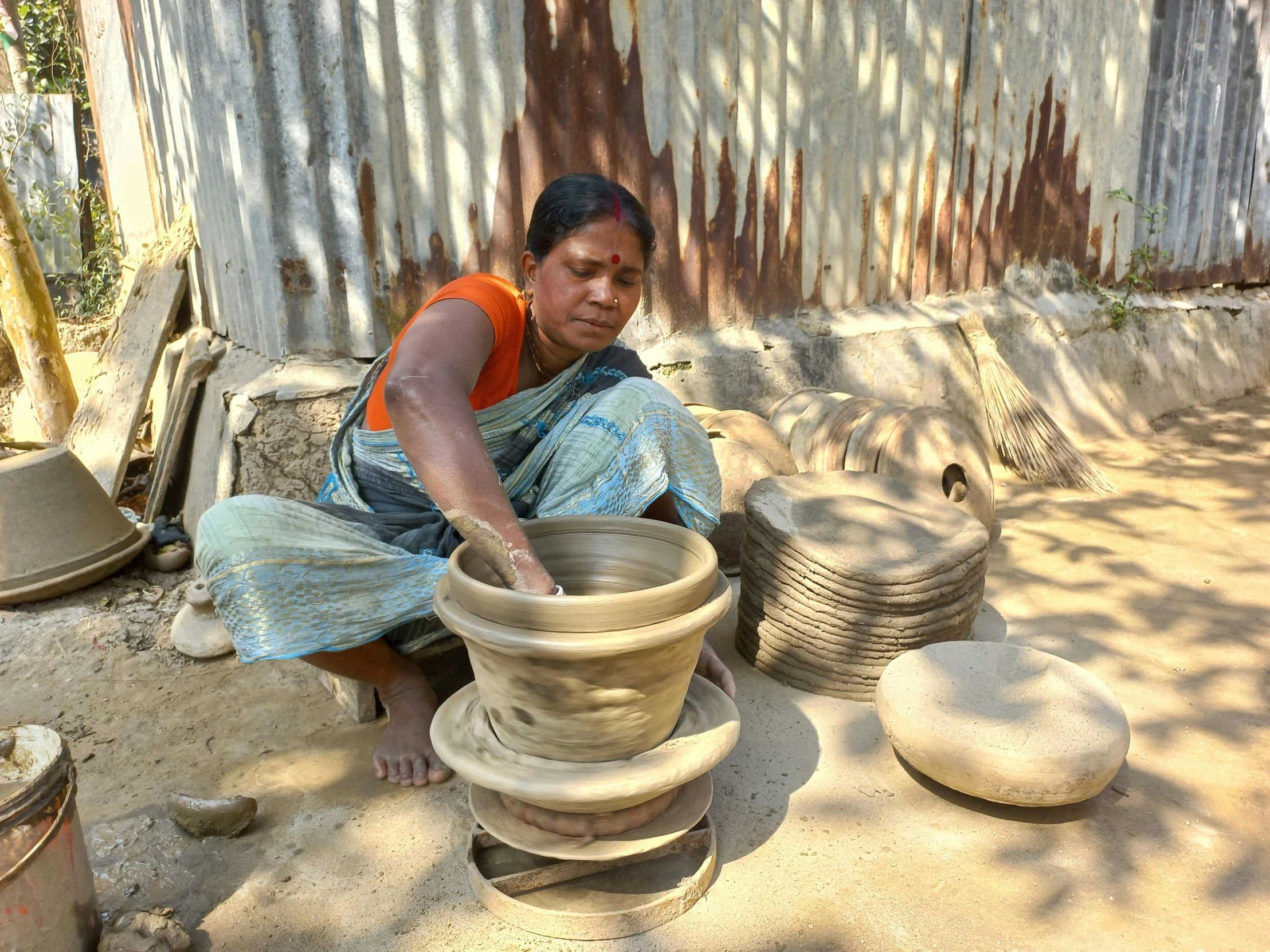 woman in blue shirt sitting by some large pottery pots