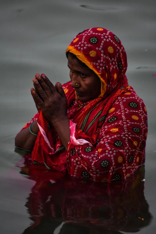 a woman in a red and yellow outfit prays in the water