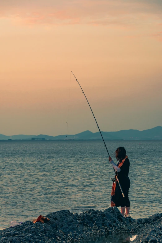 woman standing at shore fishing on lake during dusk