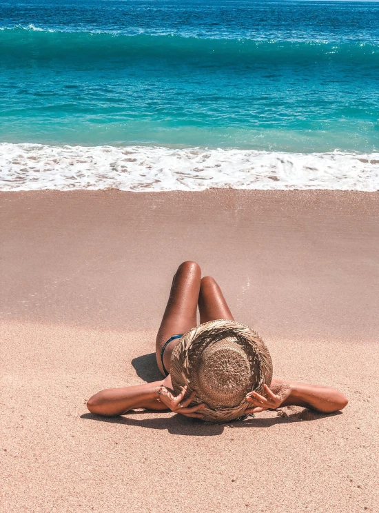 woman in a hat laying down on the sand at the beach