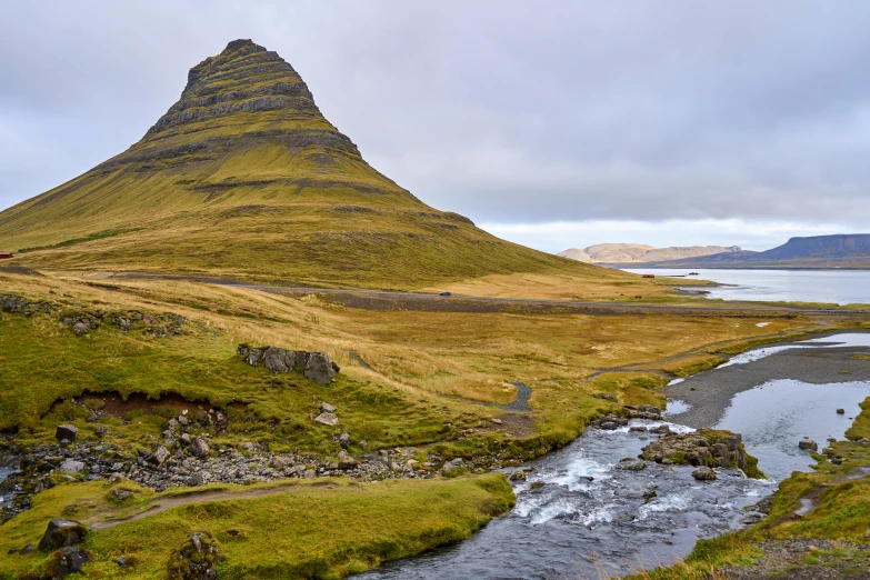 there is a grassy hill by the river and a mountain