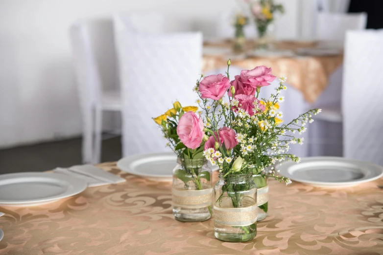 two clear vases with pink roses and yellow flowers are on a table with napkins
