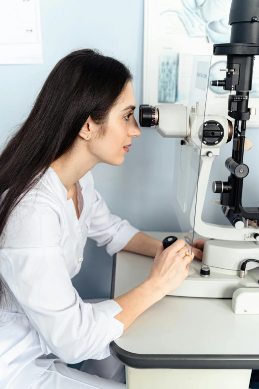 a woman sitting at a table looking through an eyepiece