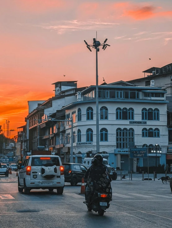 the sun sets behind several people riding a motorbike down the street