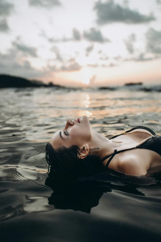 young woman wearing black swimsuit floating in water at sunset