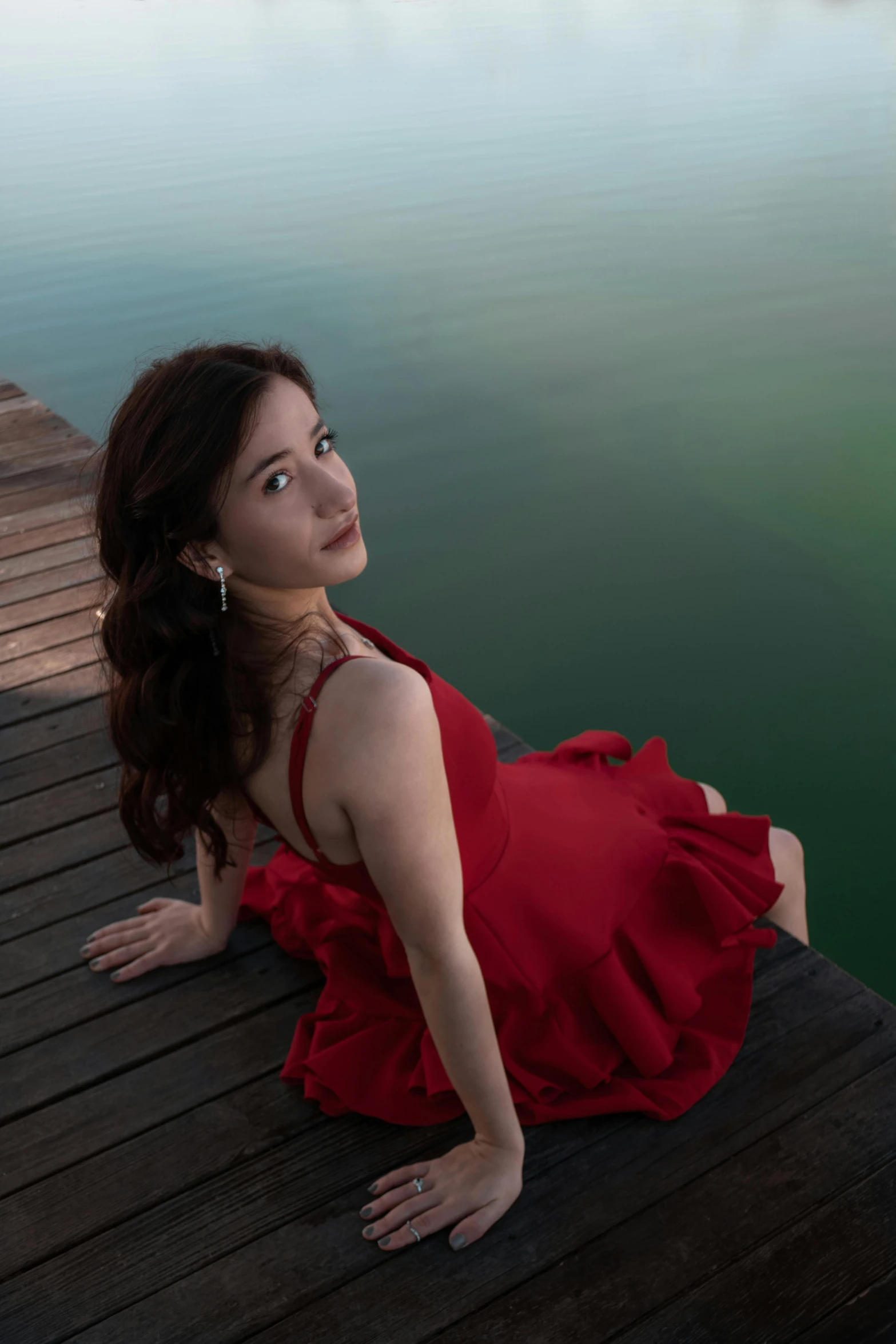 a woman in a red dress sitting on the pier looking at the water